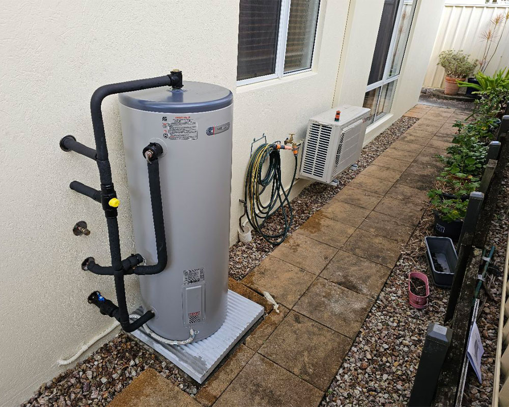Outdoor hot-water tank with insulated pipework beside a house.