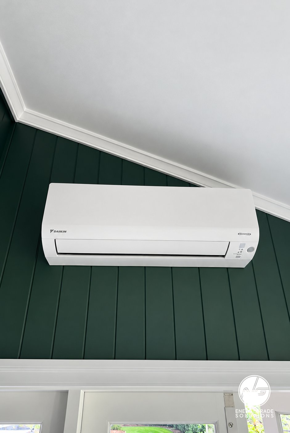 Daikin wall-mounted air conditioner installed on a green panelled wall.