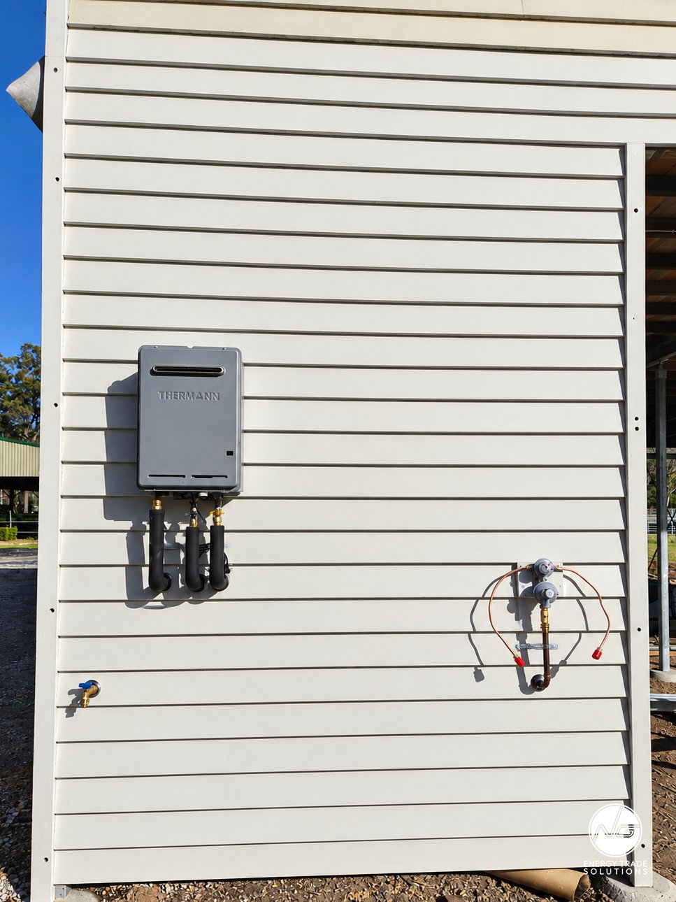 Wall-mounted Thermann instantaneous gas hot water unit with connected pipework.
