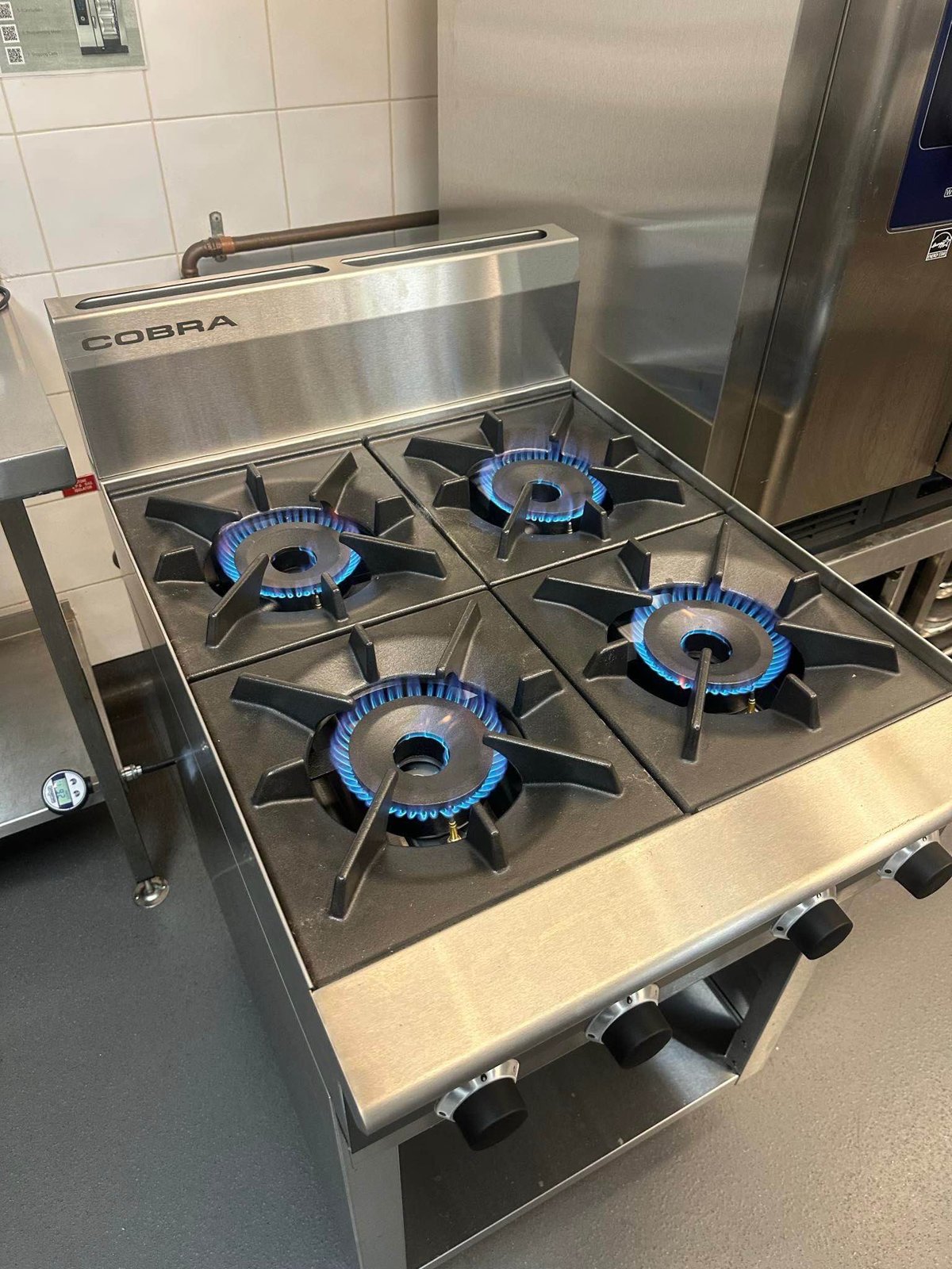 Four-burner commercial gas cooktop operating in a kitchen.