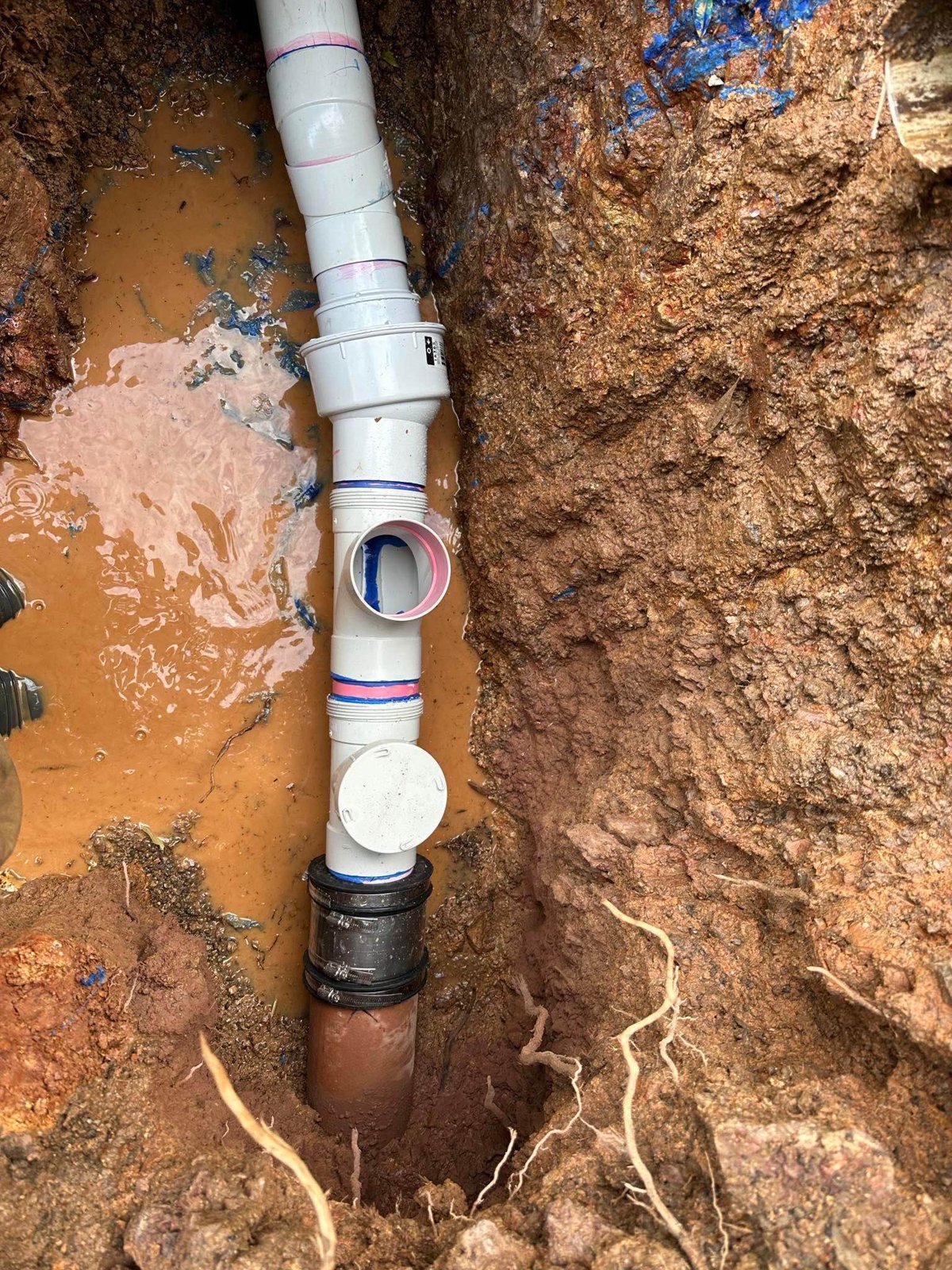 Drain repair pipework exposed in an excavated trench.