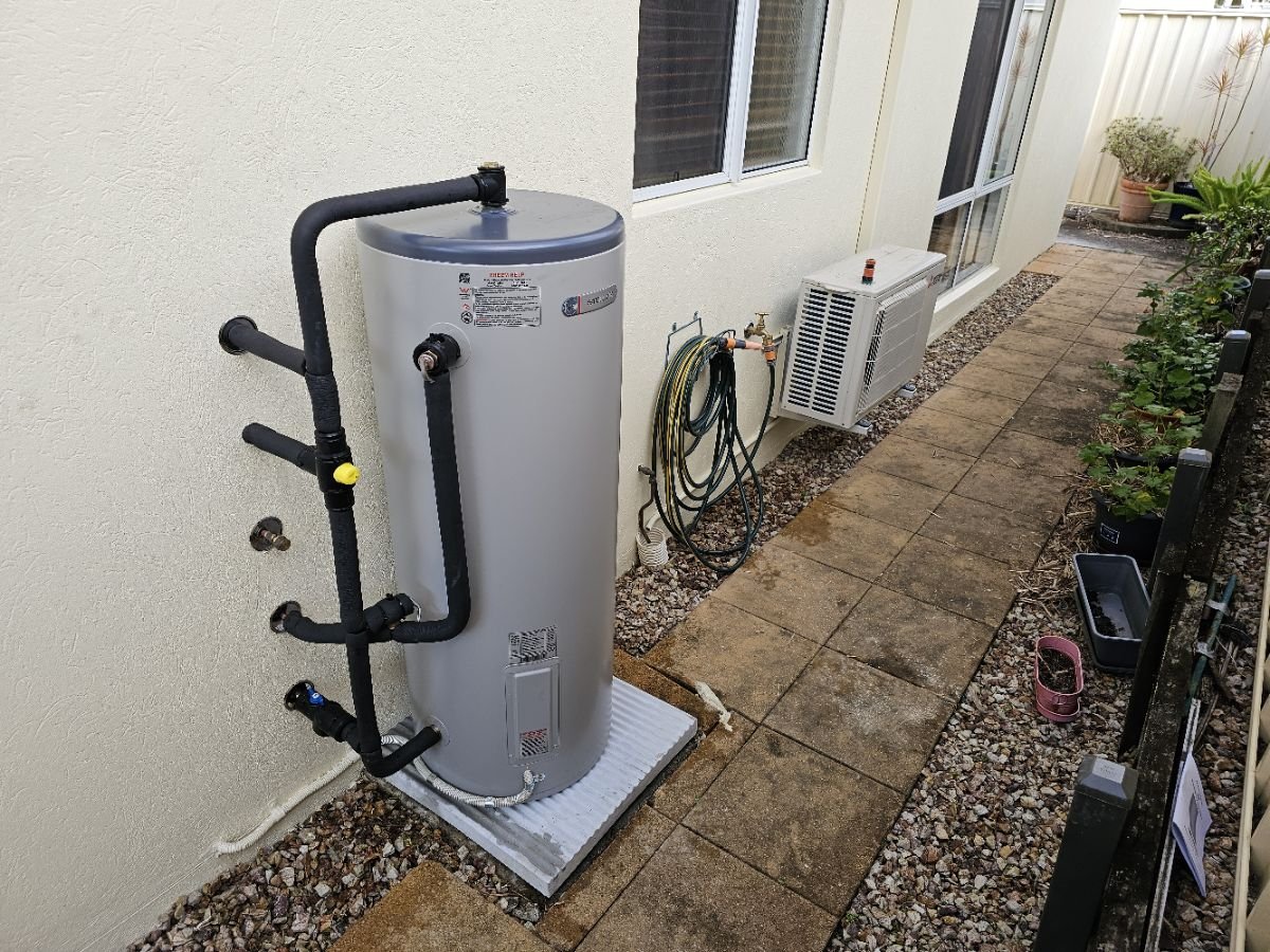 Outdoor electric hot water cylinder with connected pipework.