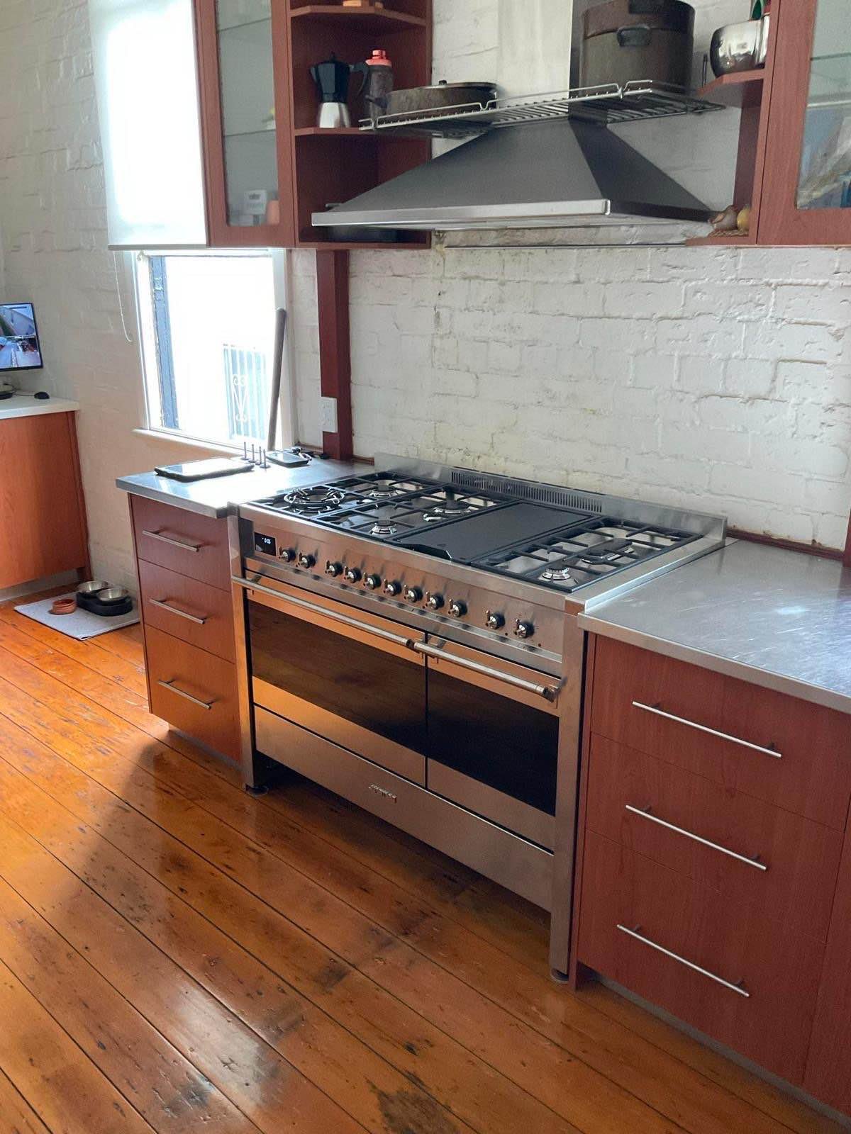 Residential gas cooker and rangehood installed in a kitchen.