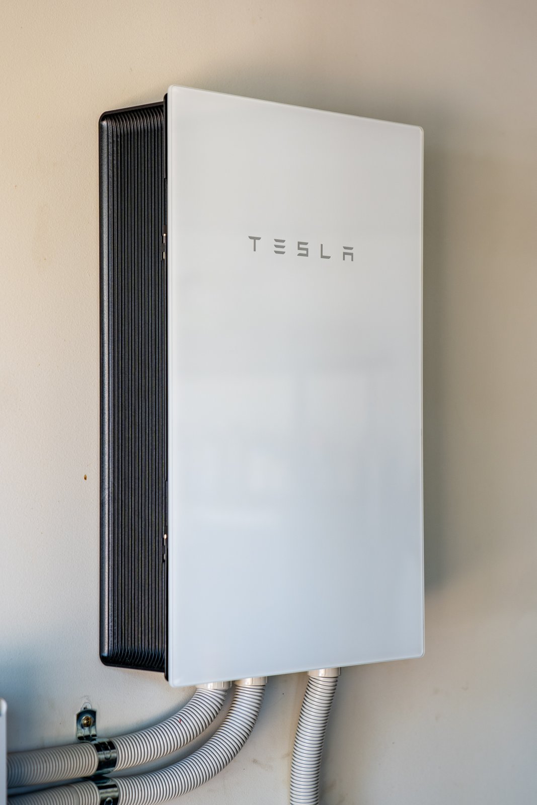 Wall-mounted Tesla home battery with connected conduit.